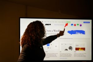Pessoa apontando para uma pagina de site exibida em tela grande durante apresentacao de design web