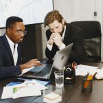 Dois empresarios discutindo e comparando opcoes de negocio com laptops e graficos