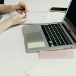 Pessoa fazendo anotacoes ao lado do notebook para planejar conteudos e prompts de marketing digital com IA