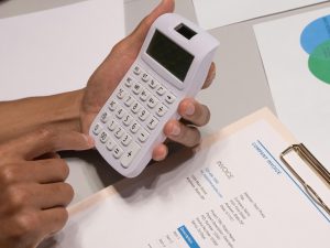 Pessoa calculando preco de produto ou servico com calculadora e documentos