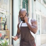 Dono de pequeno negócio falando ao celular em frente à loja local